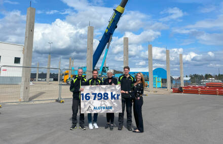 Fem personer ur Alutrades personal h&aring;ller upp skylt med beloppet f&ouml;r &aring;rets vinstdelning, framf&ouml;r byggarbetsplatsen f&ouml;r f&ouml;retagets utbyggnation av lagerlokalerna.